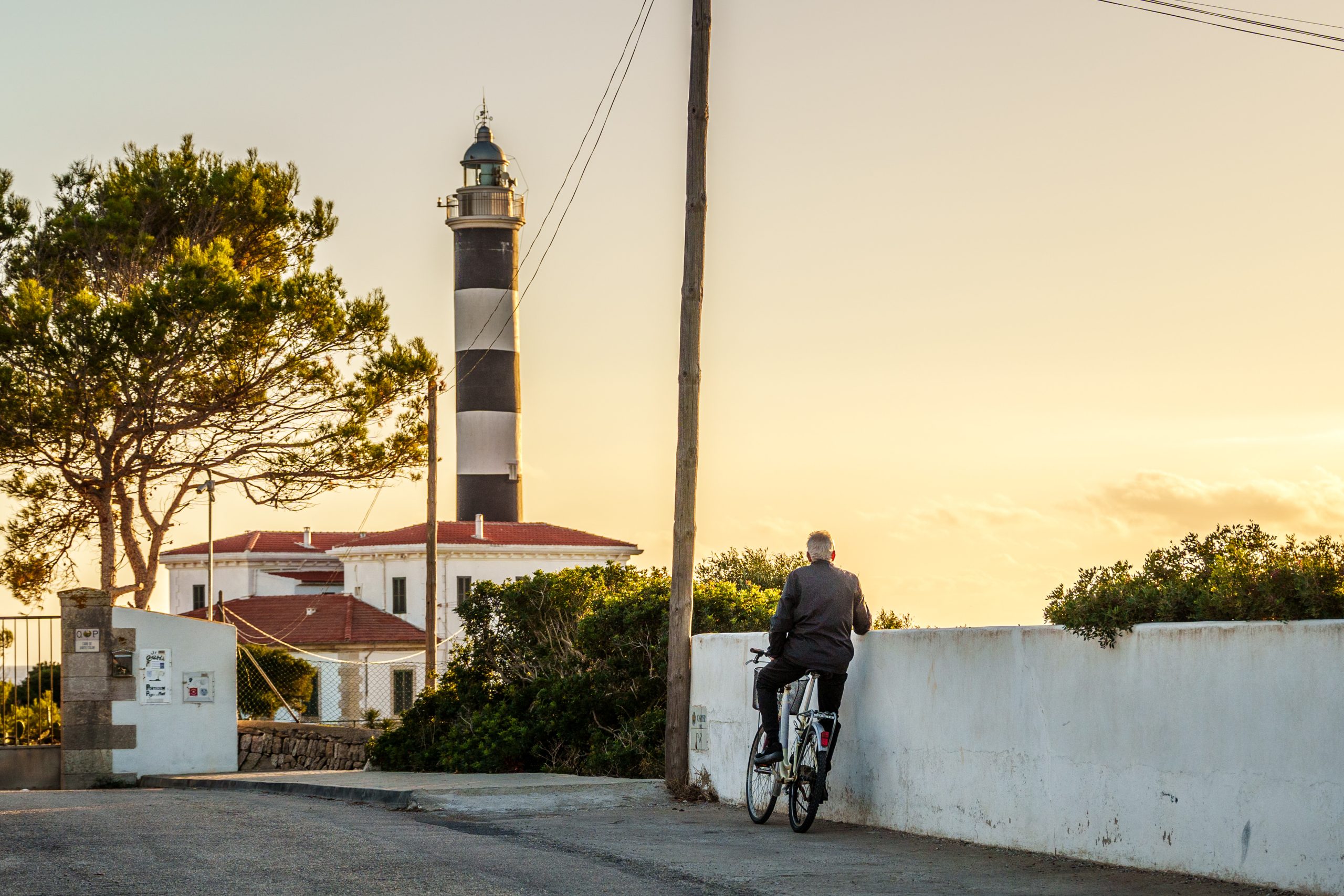 Alter Mann steht mit Fahrrad vor Leuchtturm auf Mallorca Alter Mann steht mit Fahrrad vor Leuchtturm auf Mallorca